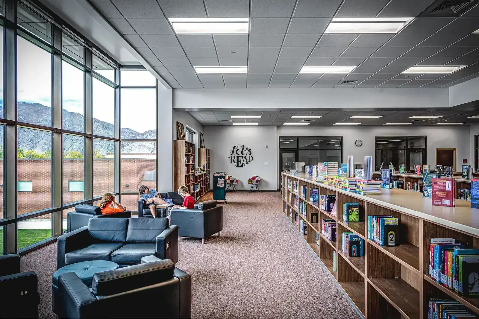 Library with wood bookshelves, blue lounge seating, students reading and tall windows looking out to the mountains.