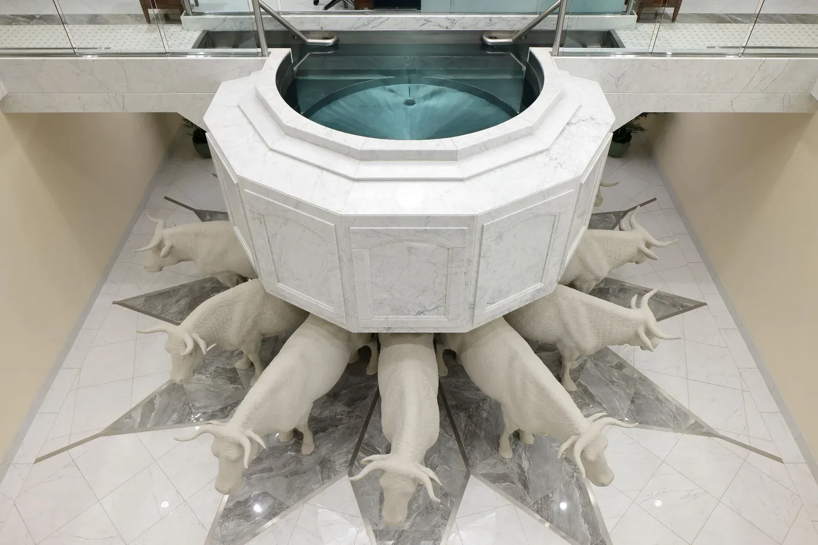 Marble baptismal font seen from above, resting on white carved oxen set into a star-patterned marble floor
