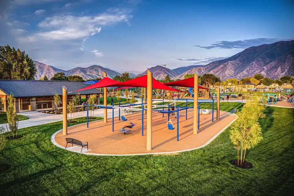 Play area under red shade sails with a bench in the foreground and mountains behind