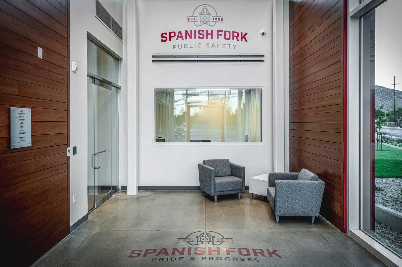 Entry lobby with wood-paneled walls, two gray armchairs and a Spanish Fork Public Safety sign above a window.