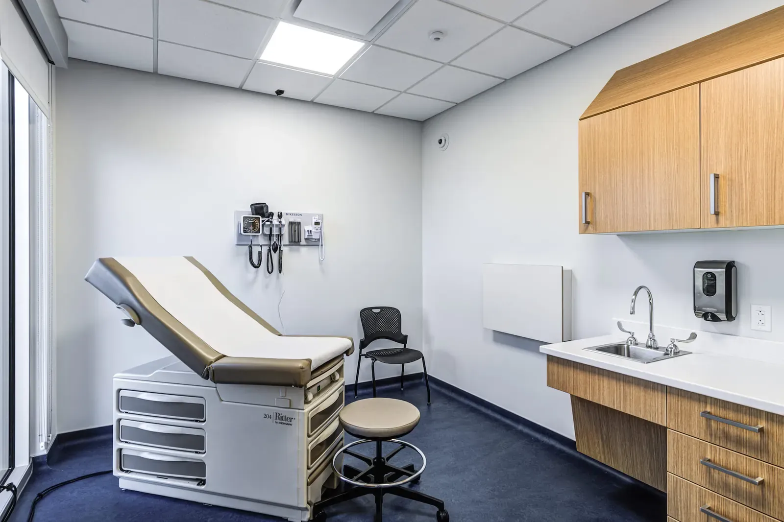 Exam room with a padded exam table, wall-mounted instruments, wood cabinets and a sink.