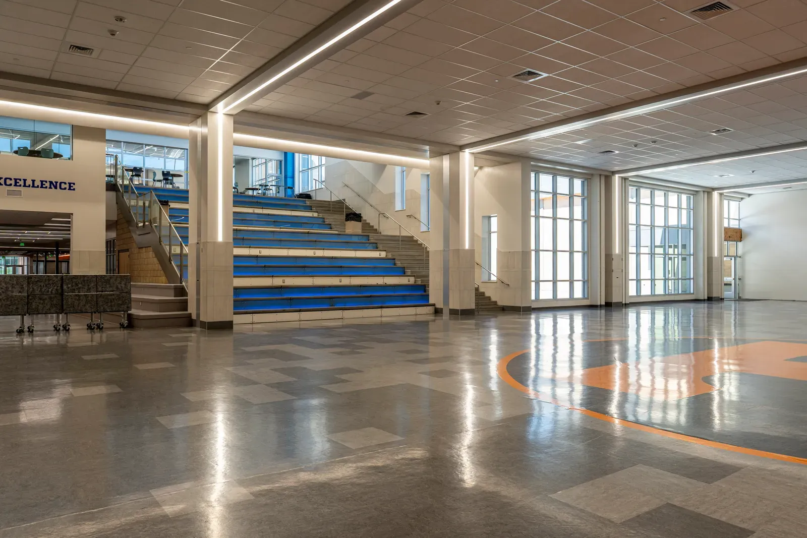 Commons with blue tiered steps, glass walls, tall windows and an orange logo on the glossy floor.