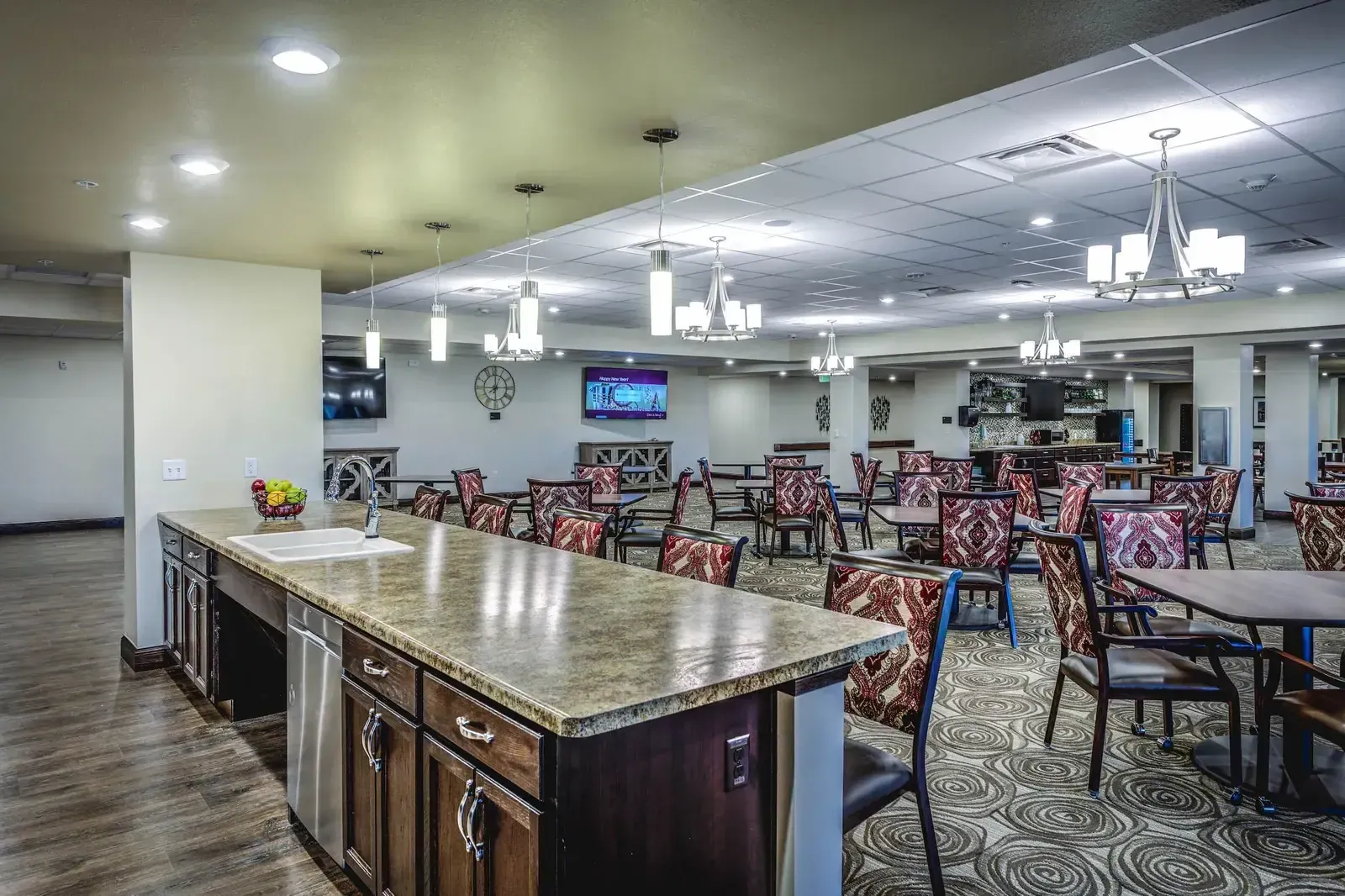 Dining hall with patterned carpet, upholstered dining chairs and a kitchen counter at left.