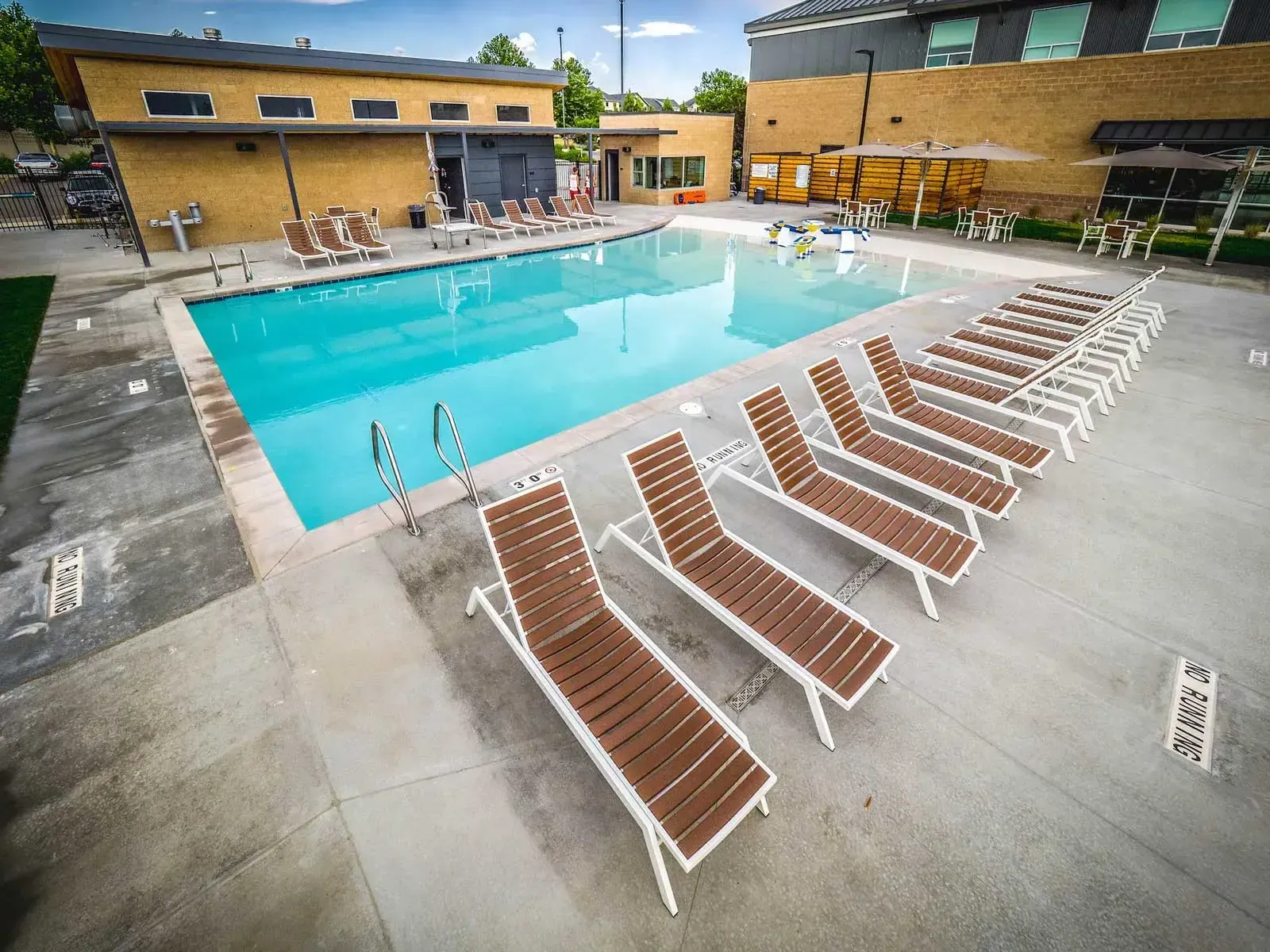 Pool deck with lounge chairs beside the water and a small building behind.
