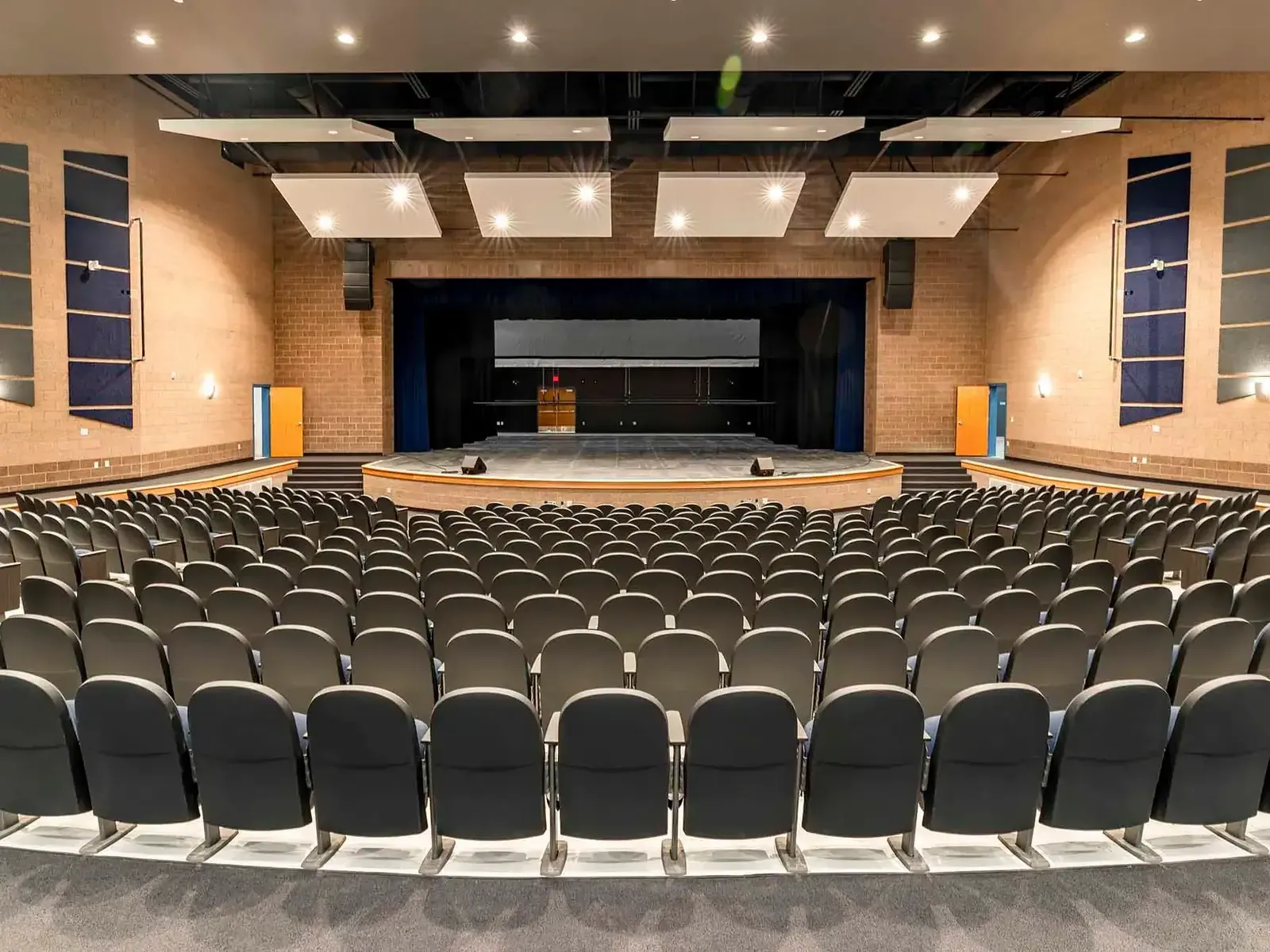 Auditorium with rows of dark seats facing a stage and wood-paneled side walls