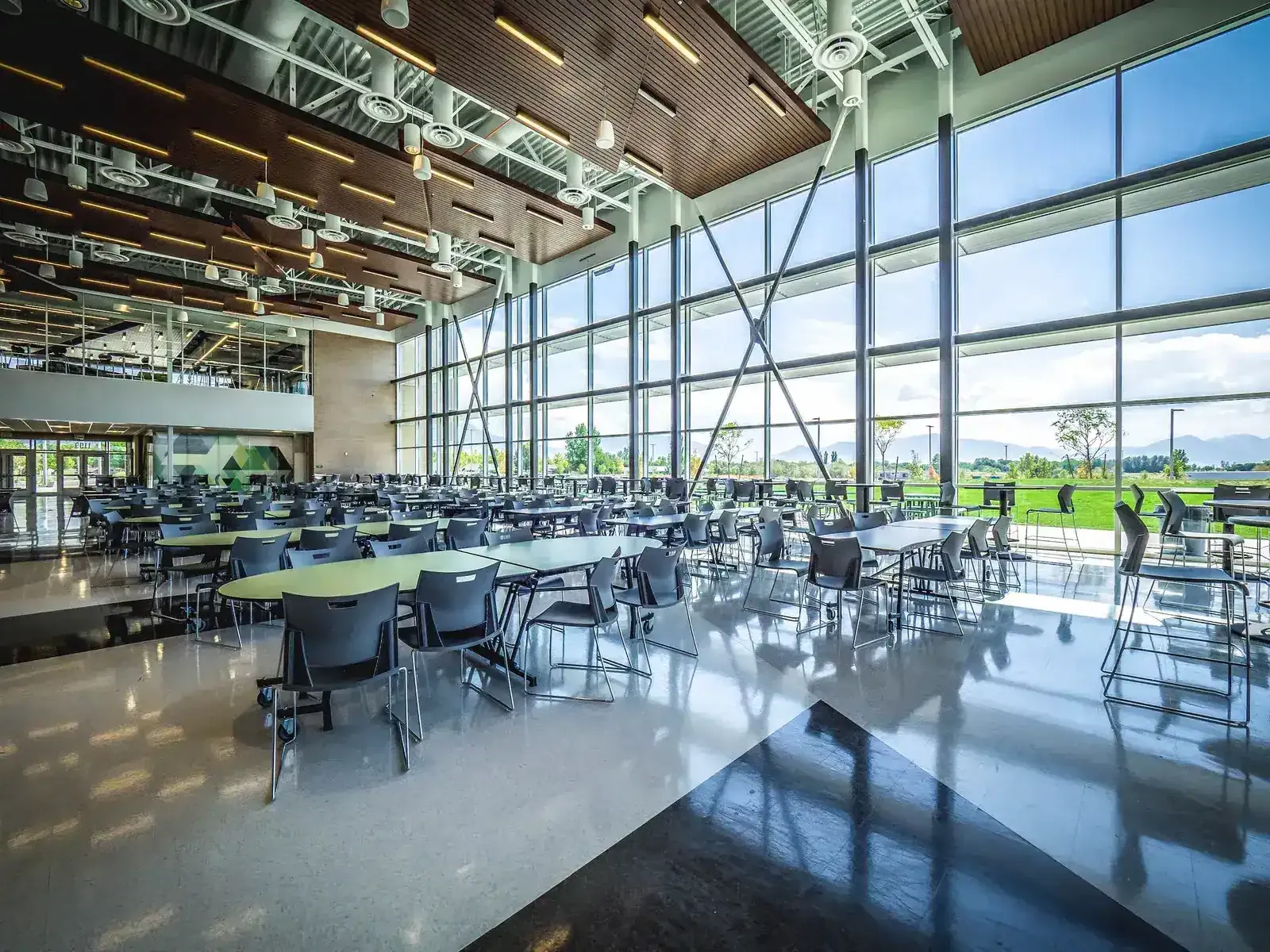 Cafeteria with rows of tables beneath a wood-slat ceiling and a tall glass wall facing the mountains