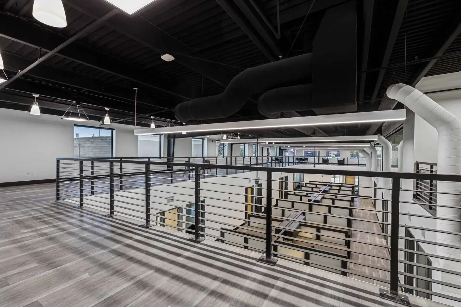 Mezzanine with a steel railing overlooking an open office floor and exposed ductwork.