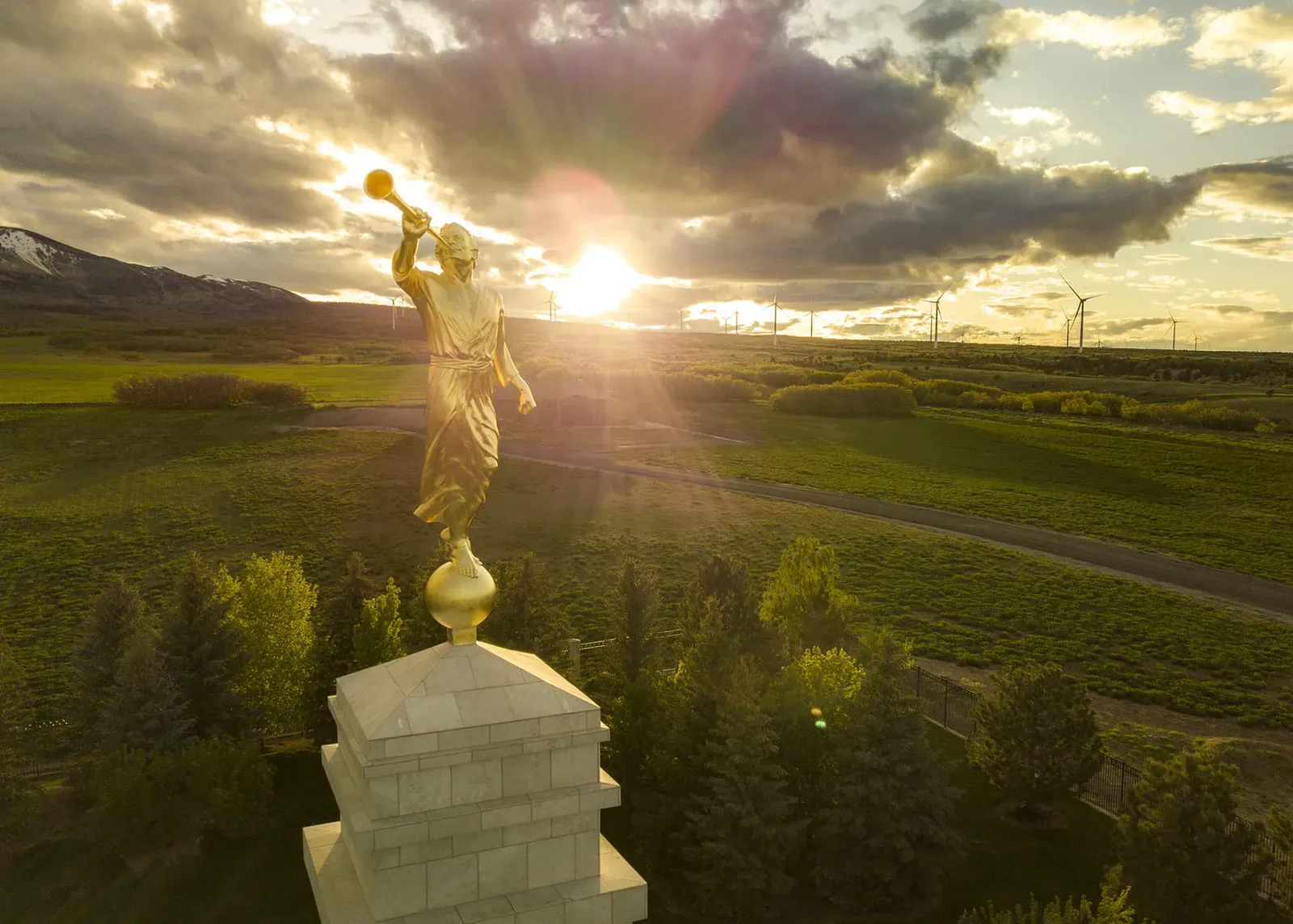 Gold statue atop the temple spire at sunset, with green fields and trees below.