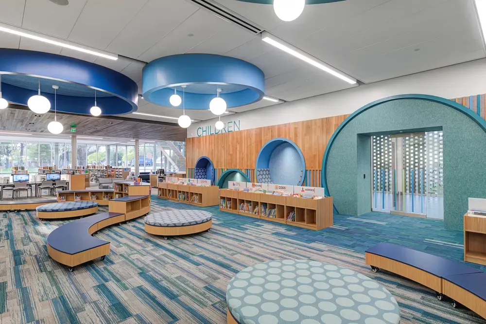 Children's area with round blue ceiling canopies, arched teal openings and low wood shelving
