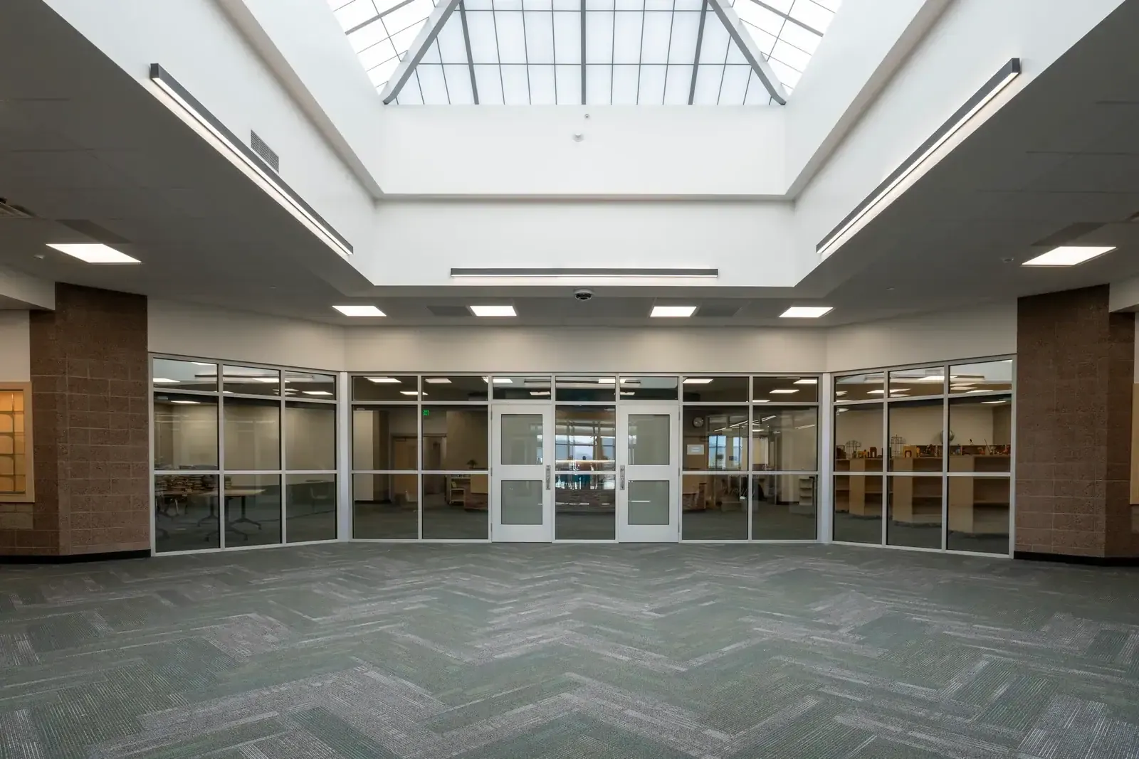 Open area under a skylight with glass walls and double doors into the rooms beyond, on patterned green carpet.