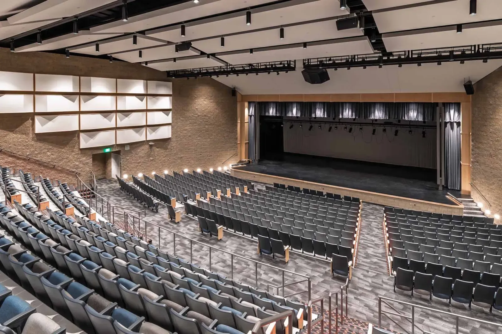 Auditorium seen from the balcony, with tiered seating, a curtained stage and acoustic wall panels.