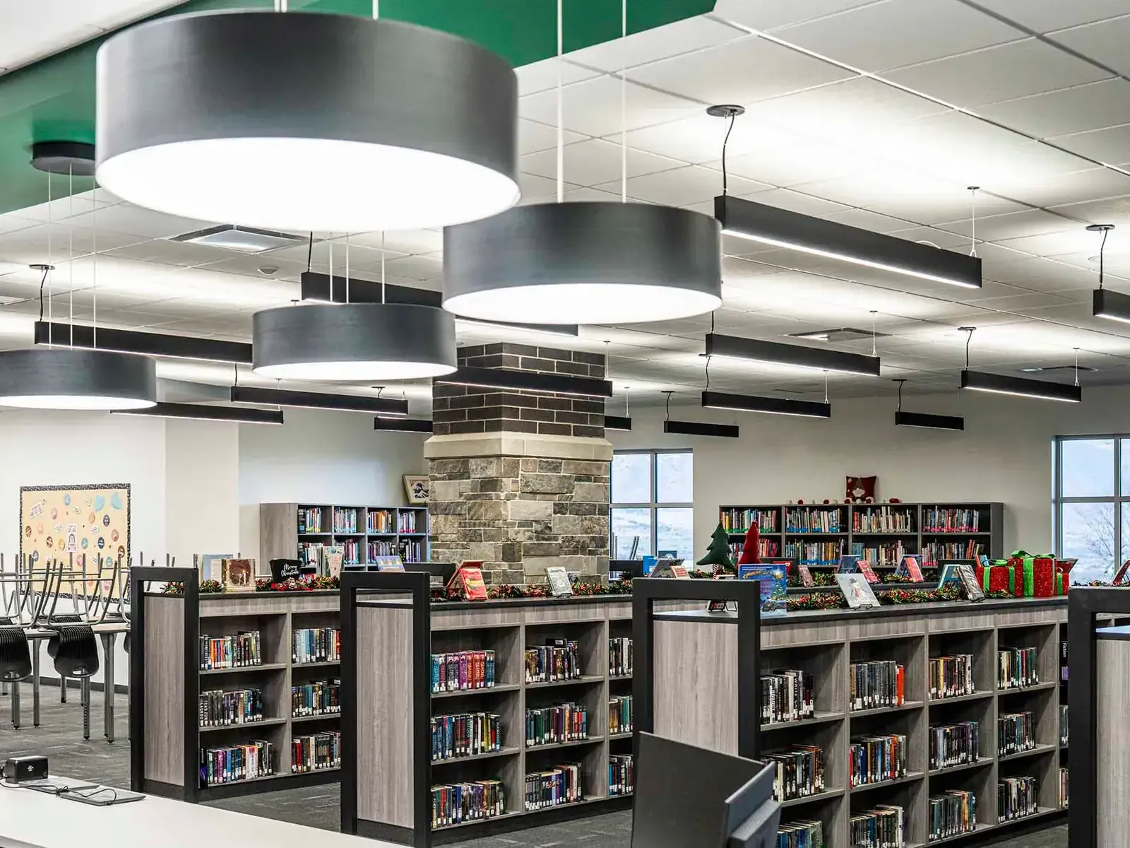Library with low wood shelving, large black pendant lights and a stone and brick column