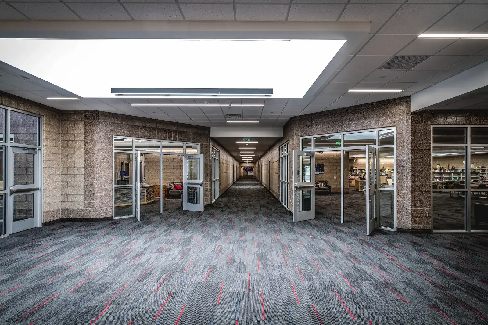 Wide carpeted corridor with glass-fronted rooms on both sides and a large ceiling light panel