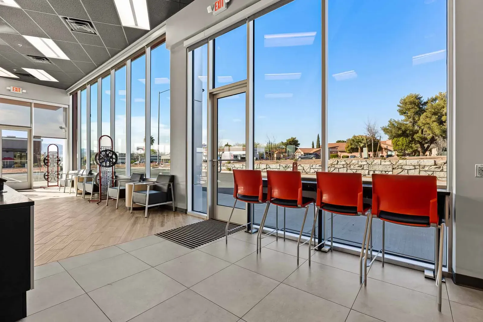 Customer waiting area with red barstools along a tall window wall and lounge chairs