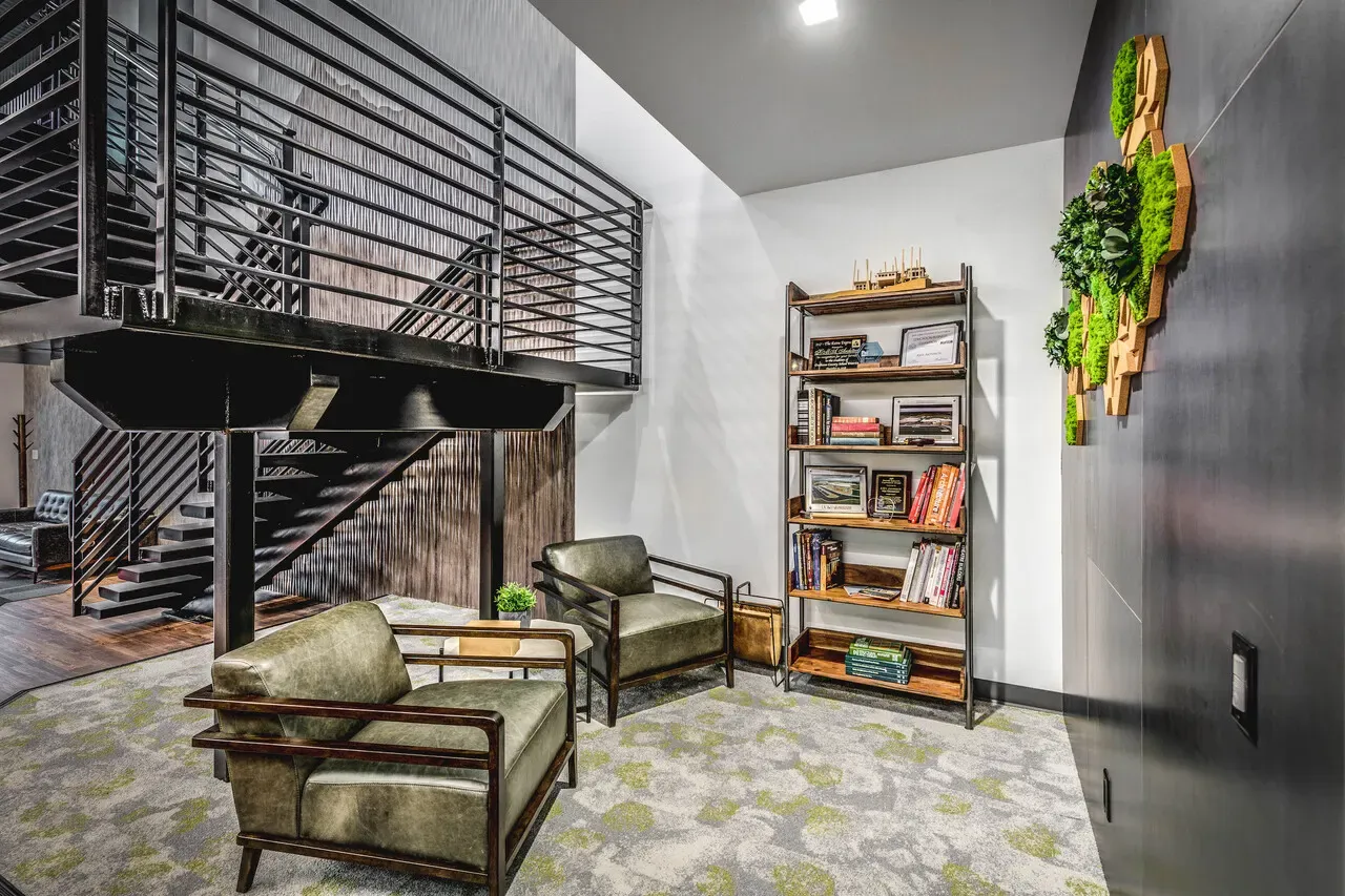 Seating nook under a steel stair with leather chairs, a bookshelf and a moss wall panel