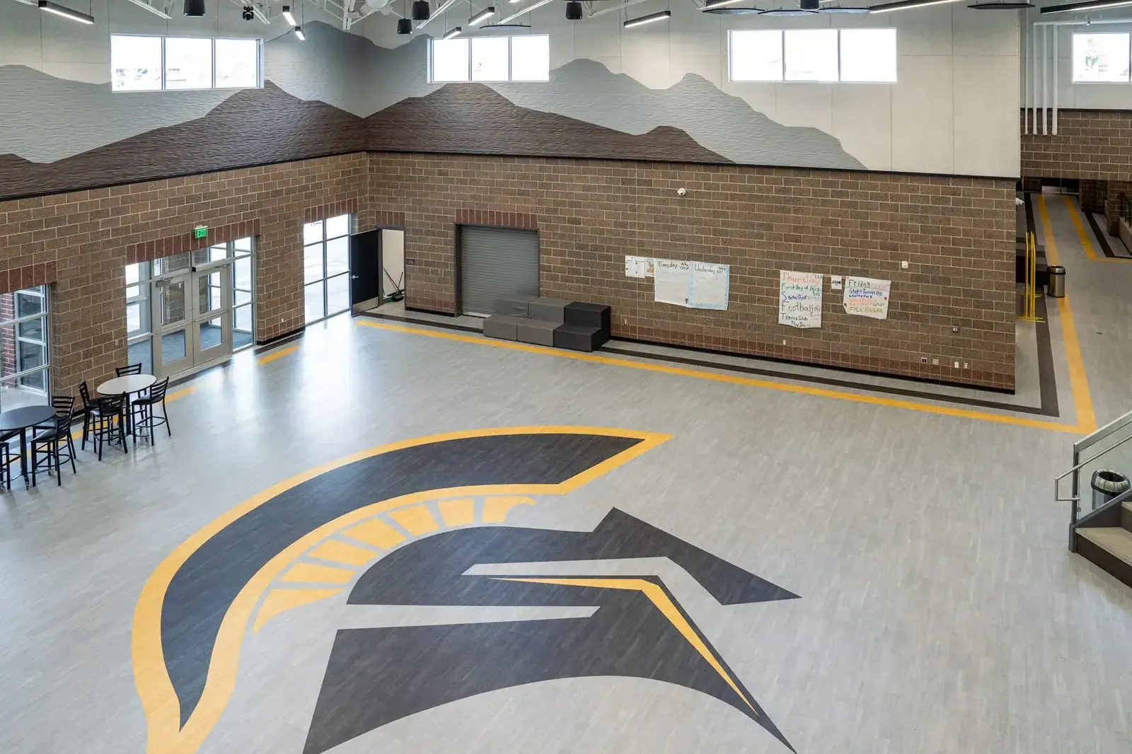 Commons seen from above, with a large Spartan helmet logo on the floor, a brick wall and a painted mountain mural.