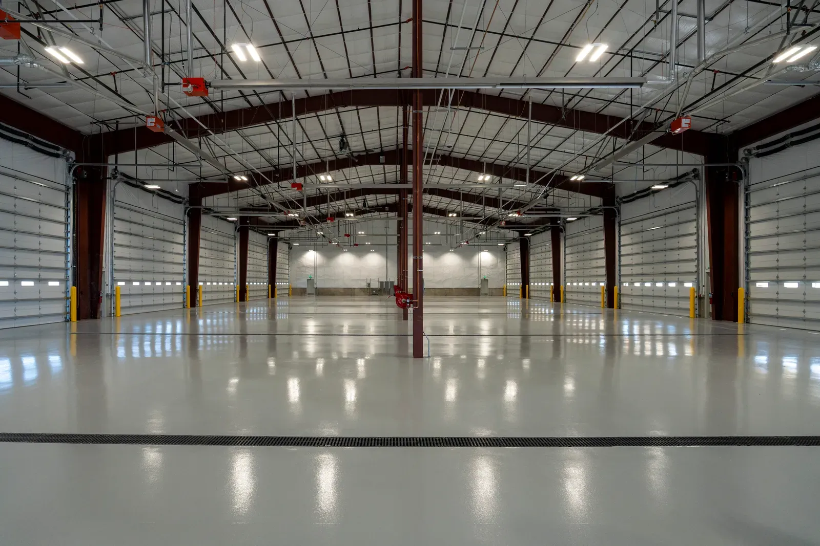 Wide equipment bay seen from the center, with overhead doors on both sides, a steel frame roof and a gray floor.