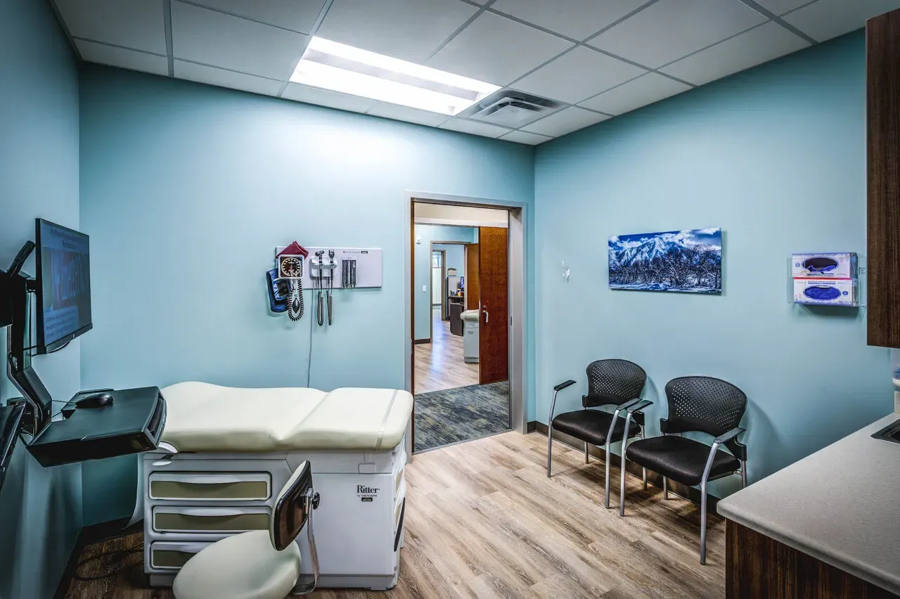 Exam room with an exam table, wall-mounted diagnostic tools and visitor chairs.