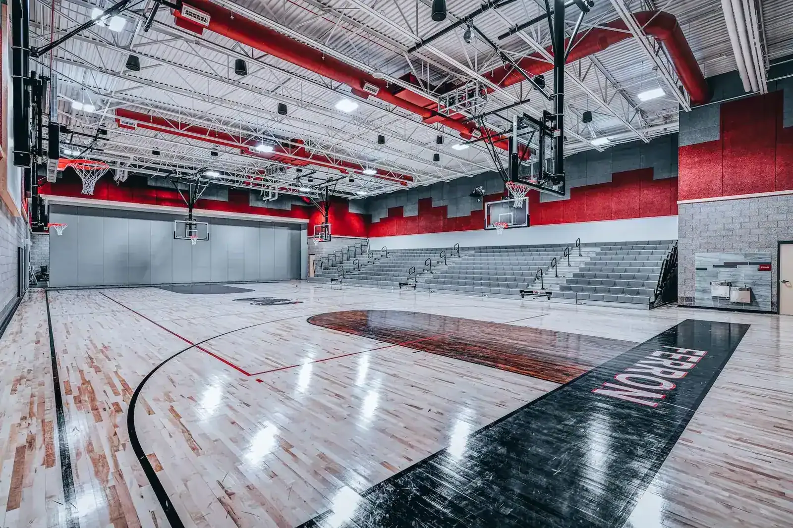 Gymnasium with a wood floor, retractable bleachers, red walls and basketball hoops