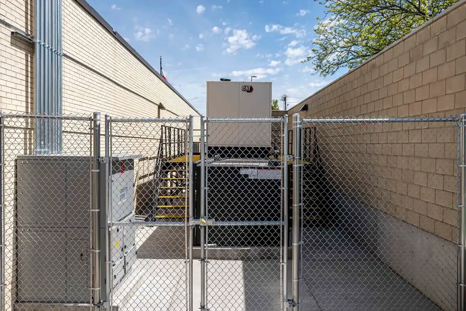 Chain-link gate and fence closing off the narrow service yard that holds the generator.