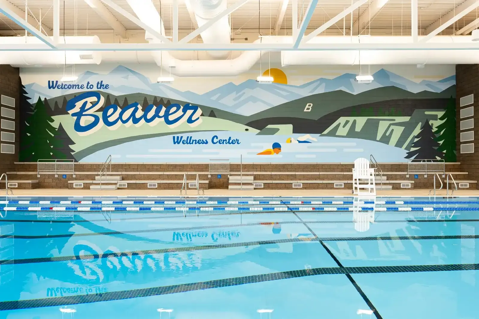 Pool with a large mural reading Welcome to the Beaver Wellness Center, showing mountains, pine trees and a swimmer.