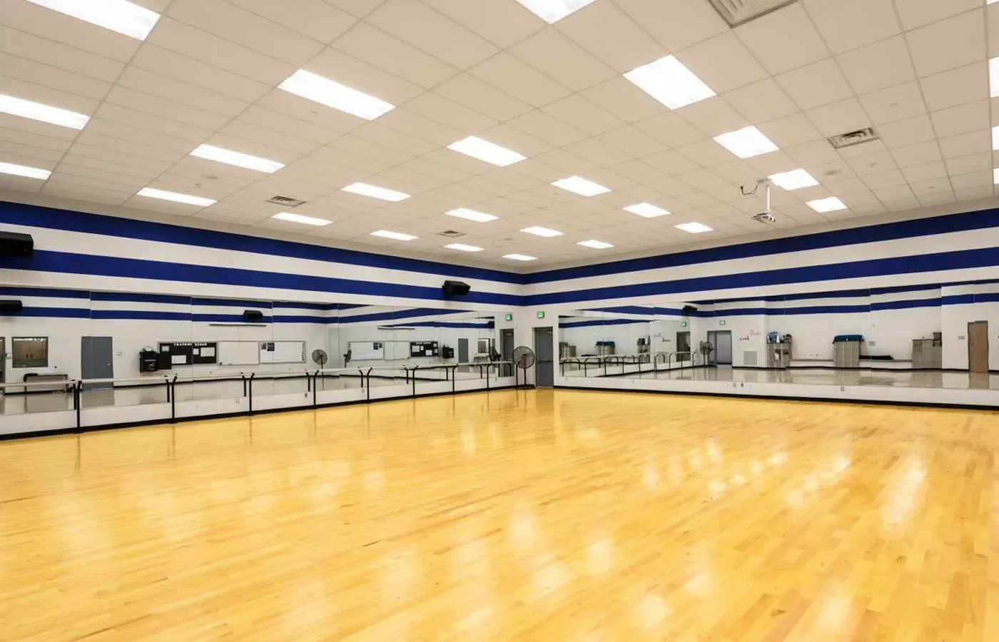 Dance studio with a wood floor, a mirrored wall with ballet barres and blue and white striped walls.