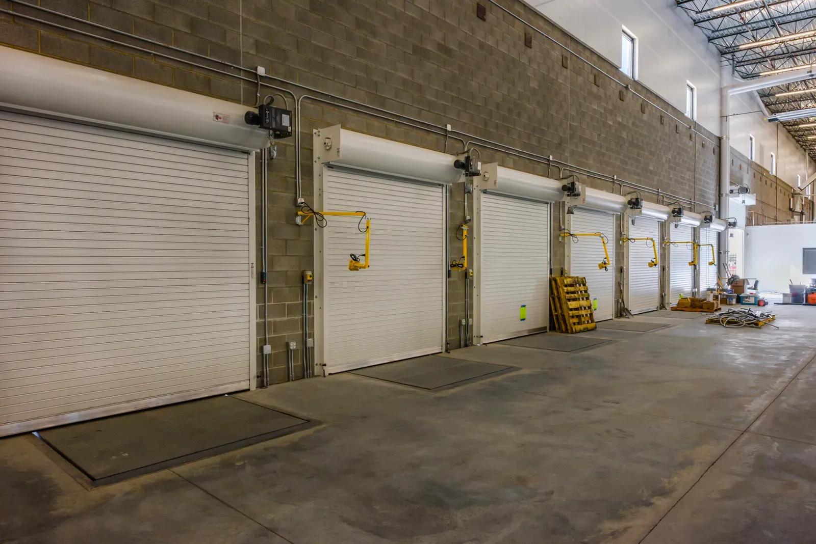 Row of roll-up dock doors with yellow equipment arms along a block wall inside the warehouse.