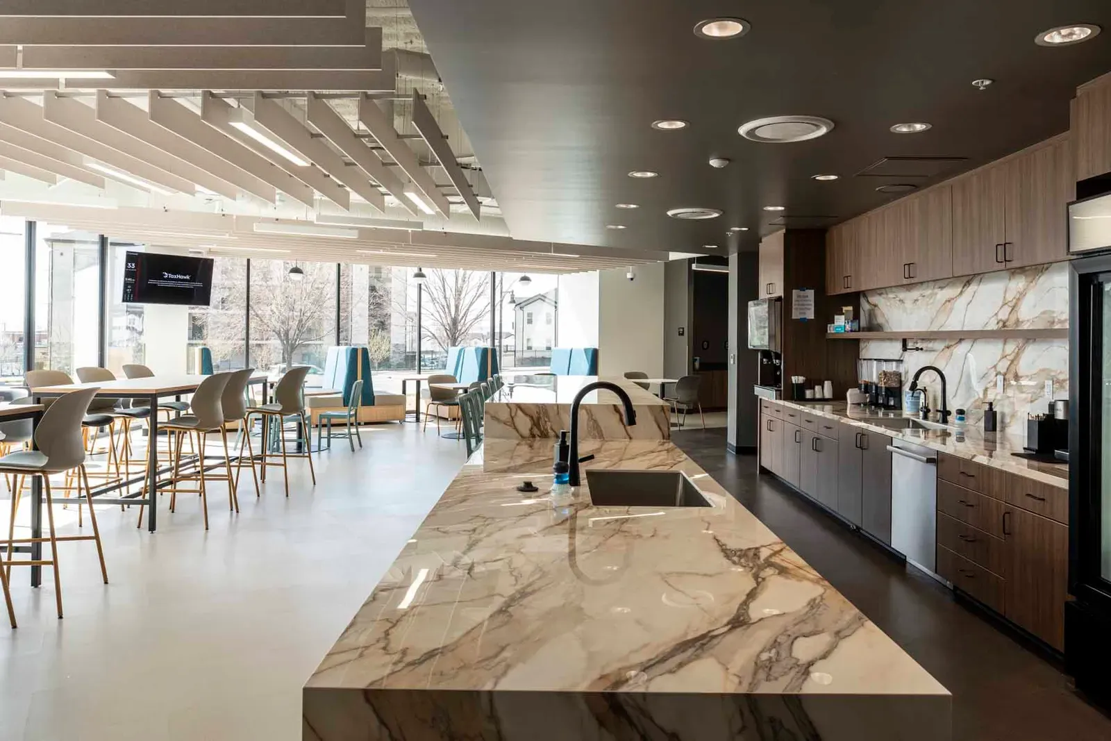 Kitchen and breakroom with a marble island, wood cabinets, and high-top tables by the windows.
