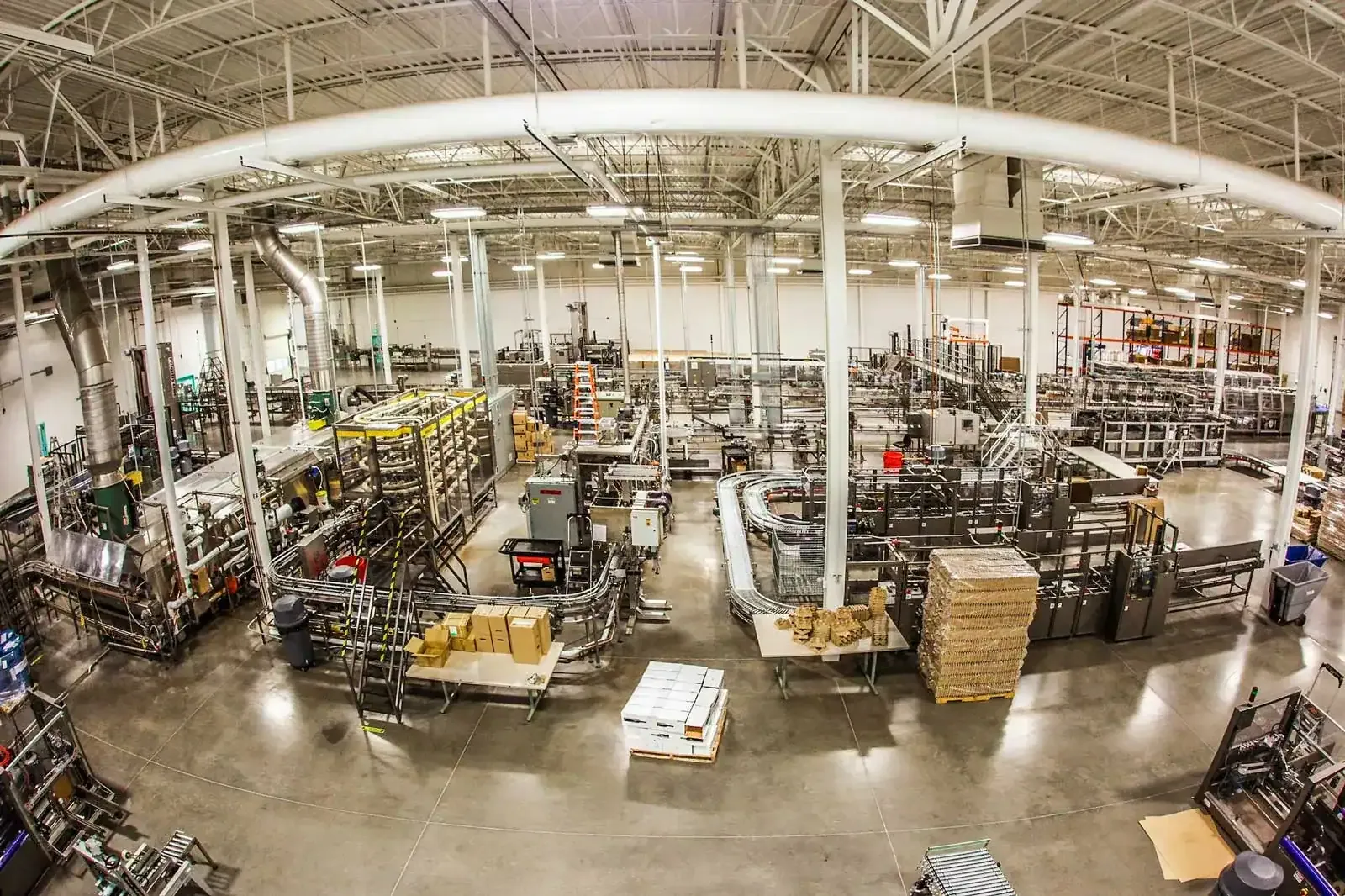 Wide view of the production floor with conveyors, equipment and overhead piping.