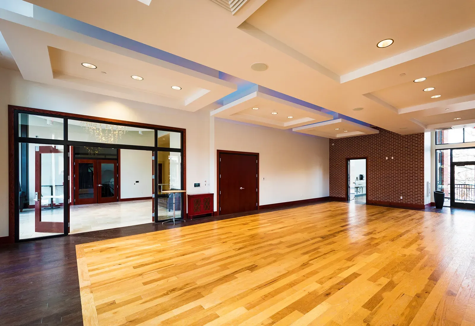 Event room with a wood floor, a brick accent wall, glass doors and blue lighting in the ceiling.