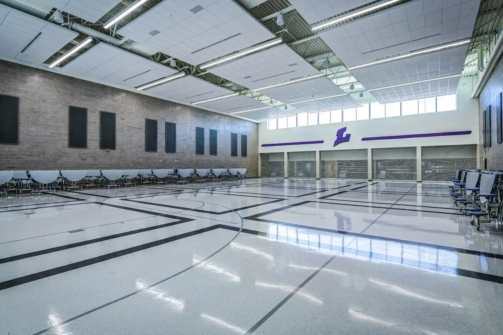 Large hall with a polished floor and a purple school logo on the wall.