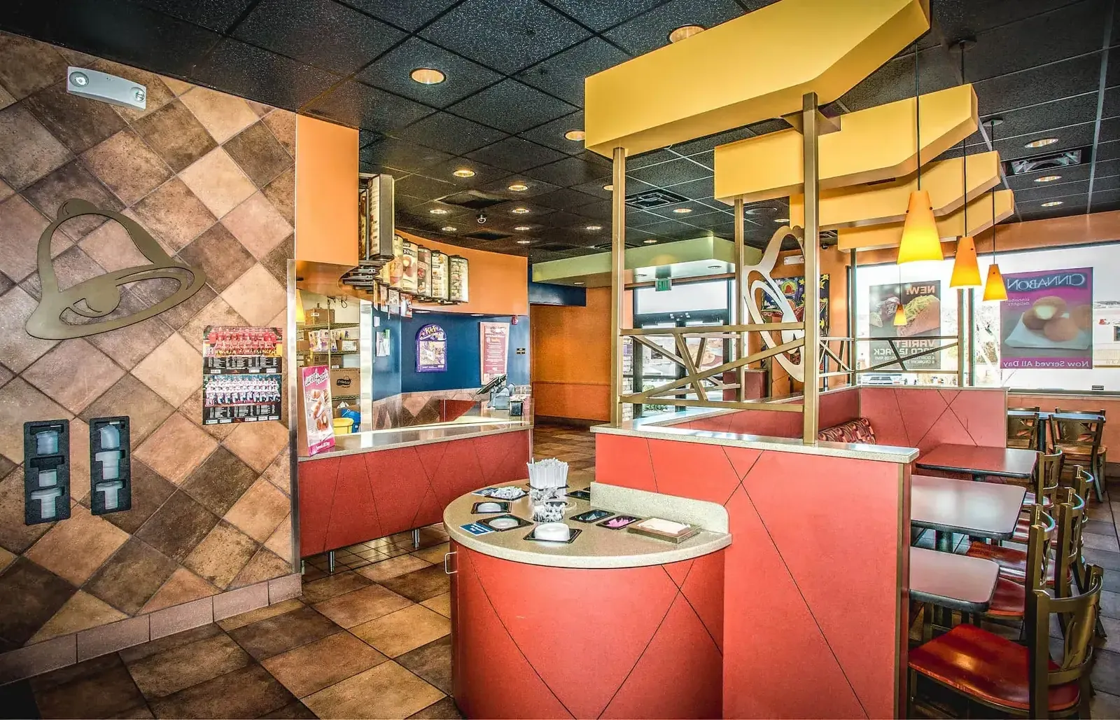 Dining room and service counter with diamond-pattern tile walls, a bell logo on the wall and red booths.