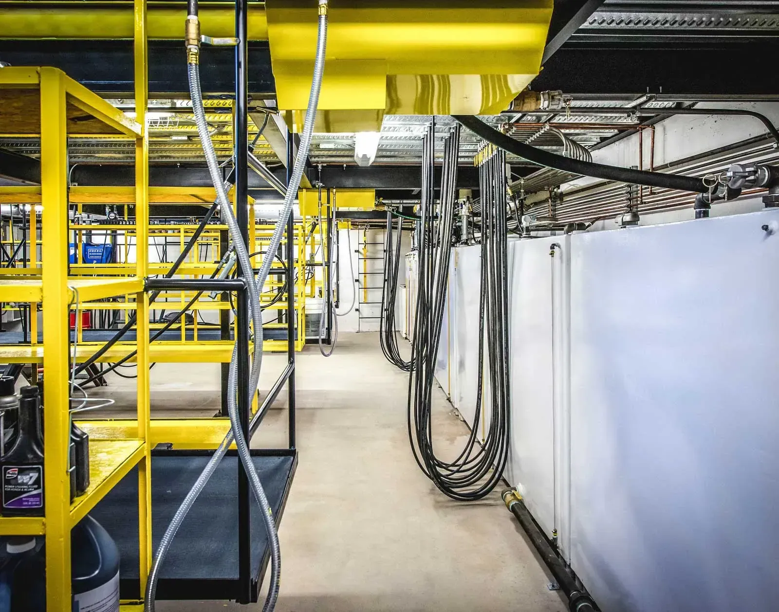 Basement corridor with hanging hoses, yellow platforms and white wall panels.