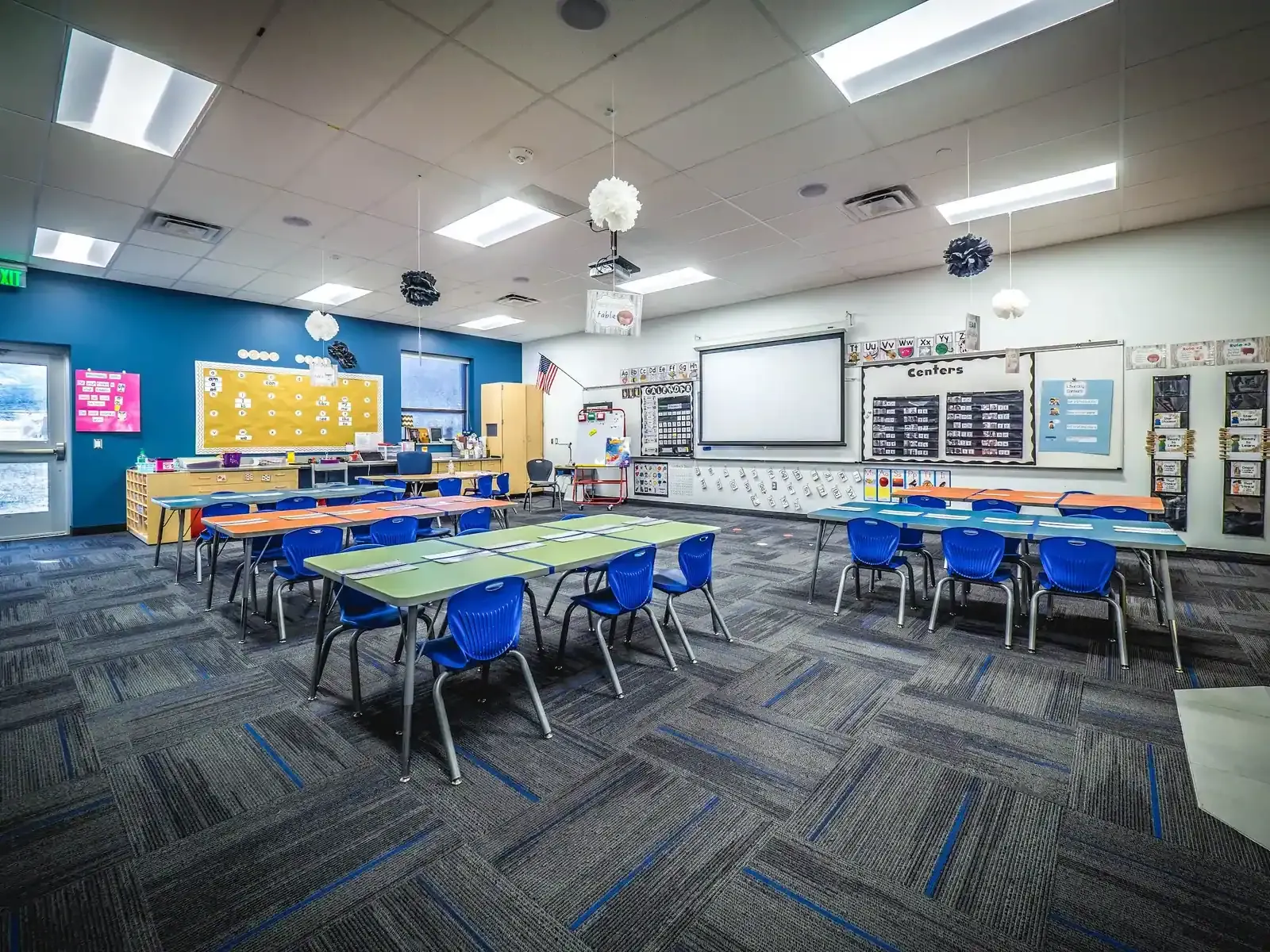 Classroom with blue chairs, group tables, a projector screen, and a blue accent wall