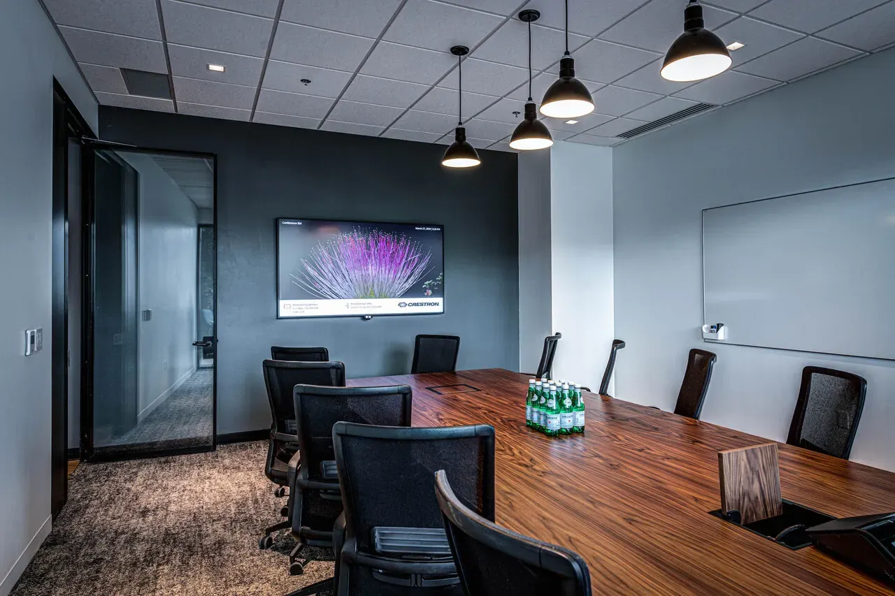 Conference room with a long wood table, black chairs and a wall-mounted display.