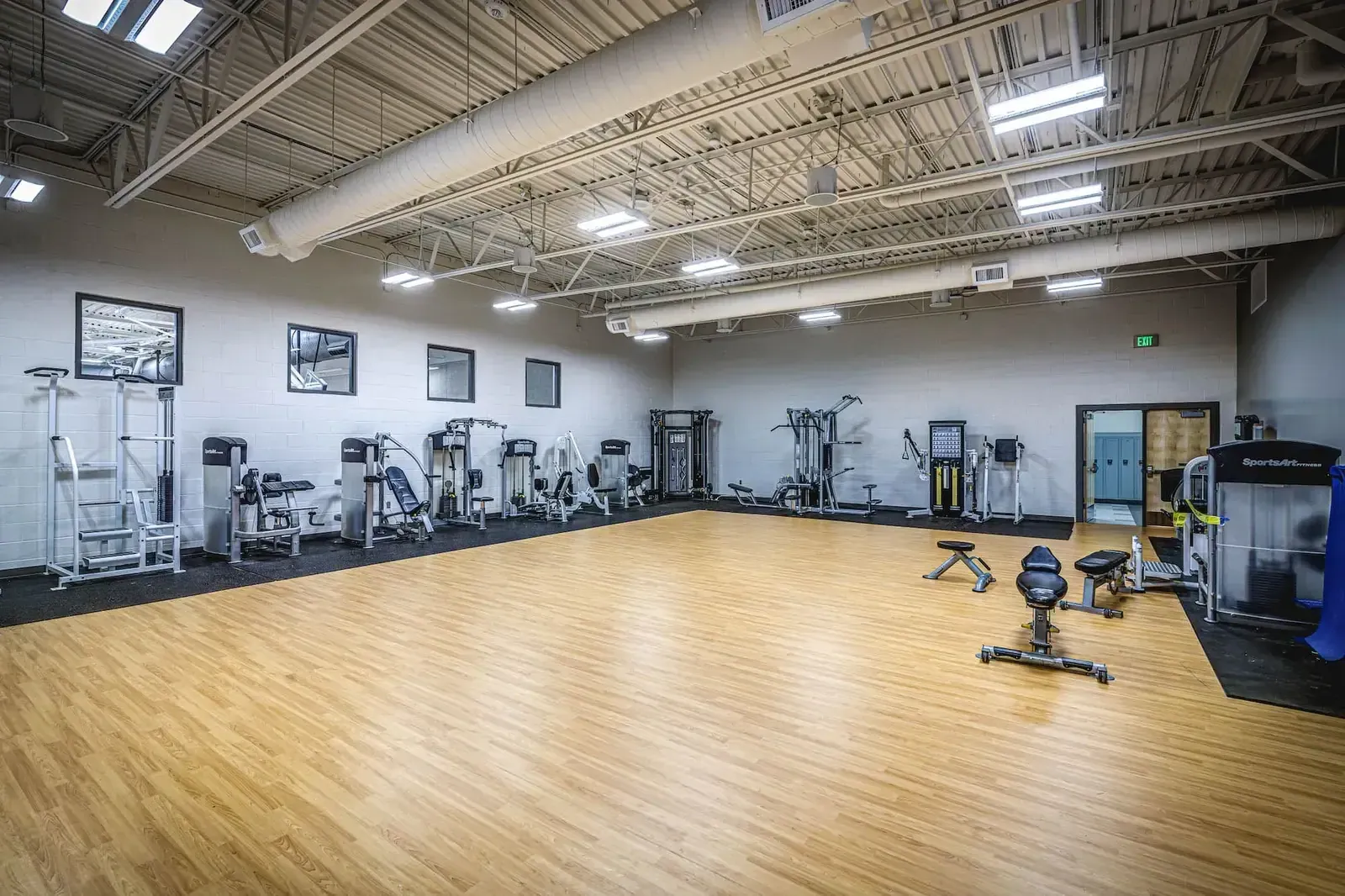 Fitness room with weight machines along one wall and a wood-floored open area.