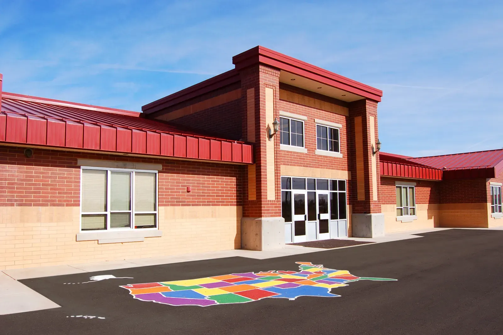 School entry with red brick and a red metal roof, and a colorful map of the United States painted on the asphalt playground.