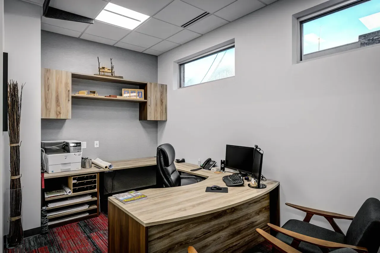 Private office with a curved wood desk, wall shelving and a narrow window