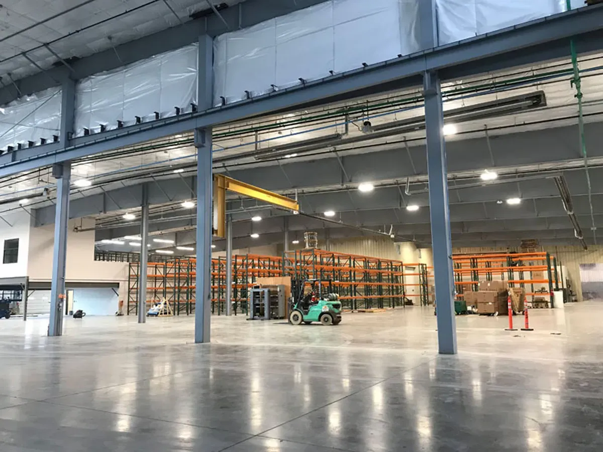 Warehouse interior with steel columns, orange pallet racking, a yellow jib crane and a forklift.