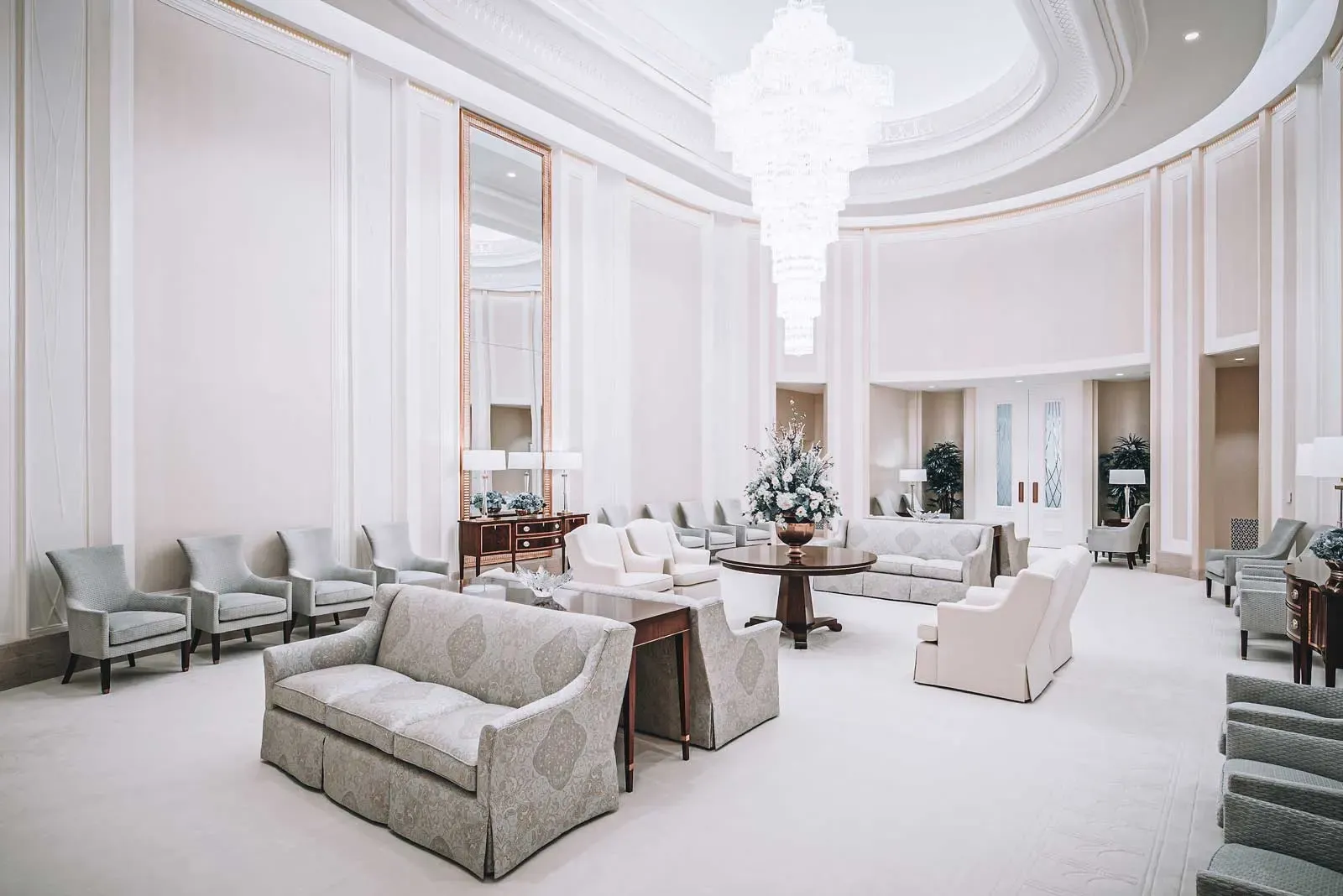 Round lounge with upholstered sofas and chairs, a round table with flowers, and a large chandelier