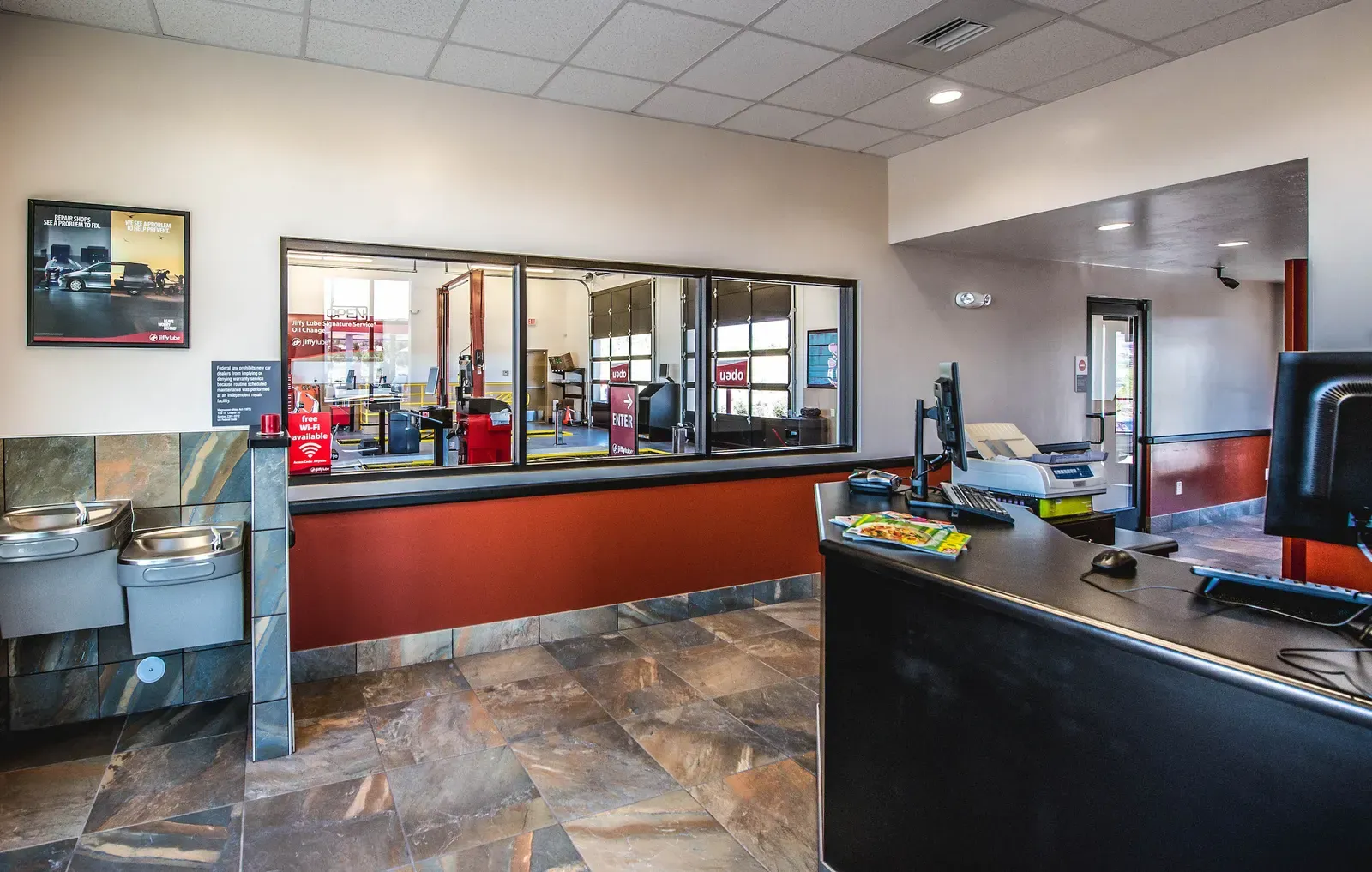 Reception area with a service-bay viewing window above a red wall and a drinking fountain at left.