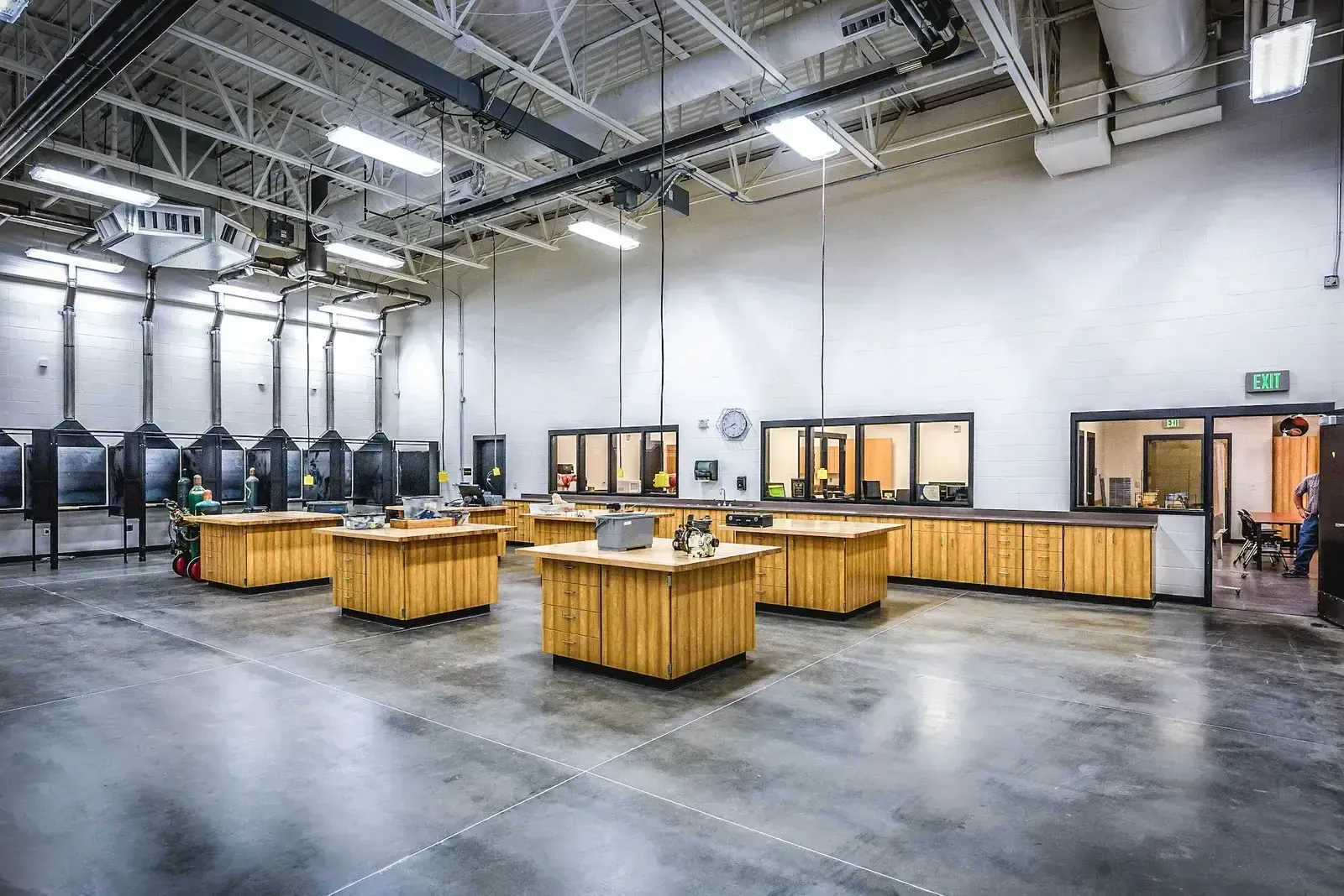 Large shop classroom with wood workbenches, a concrete floor and exposed steel framing.