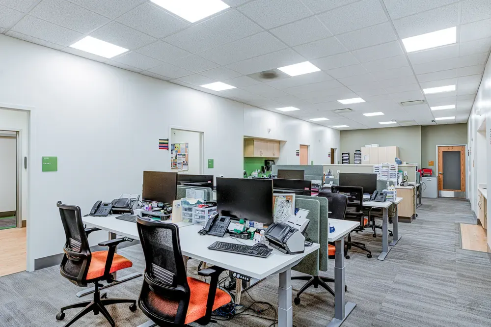 Open office area with rows of desks, computers and orange task chairs.
