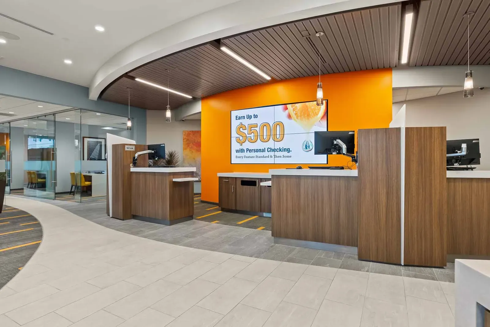 Teller counters in front of an orange wall with a screen, under a curved wood-slat ceiling.