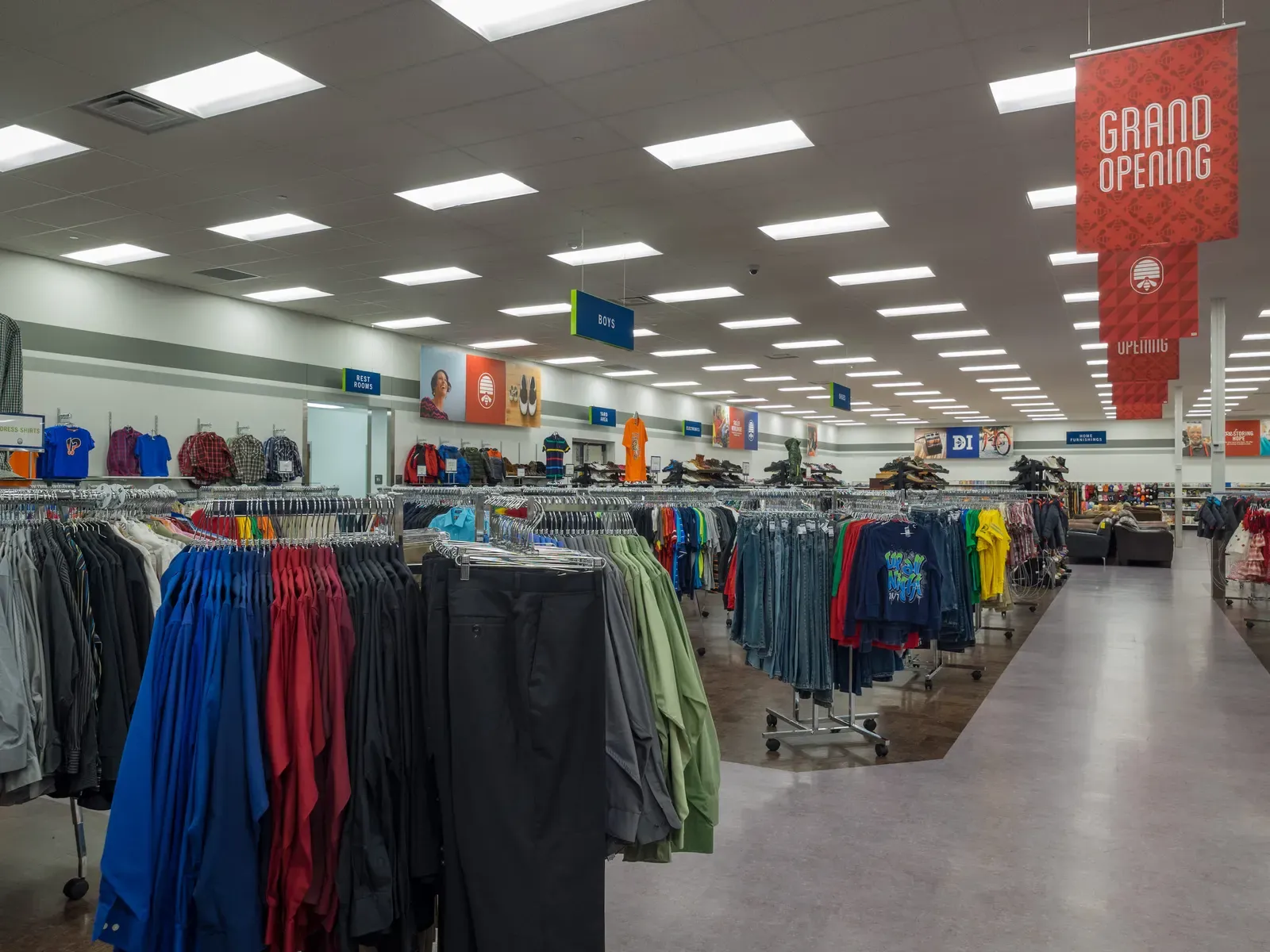 Racks of clothing on the sales floor with a red grand opening banner hanging overhead.