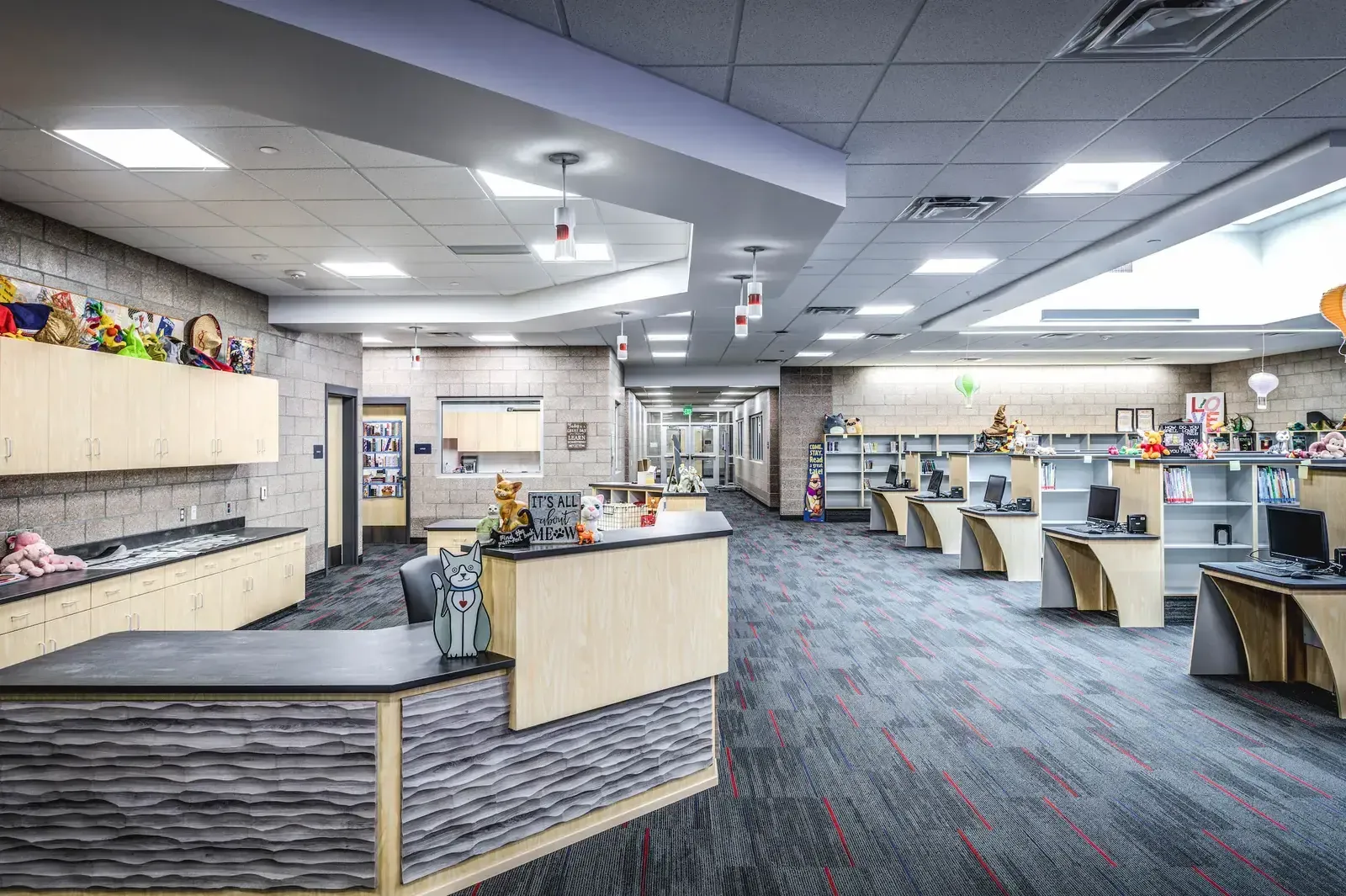 Media center with a circulation desk topped with stuffed animals and rows of computer desks