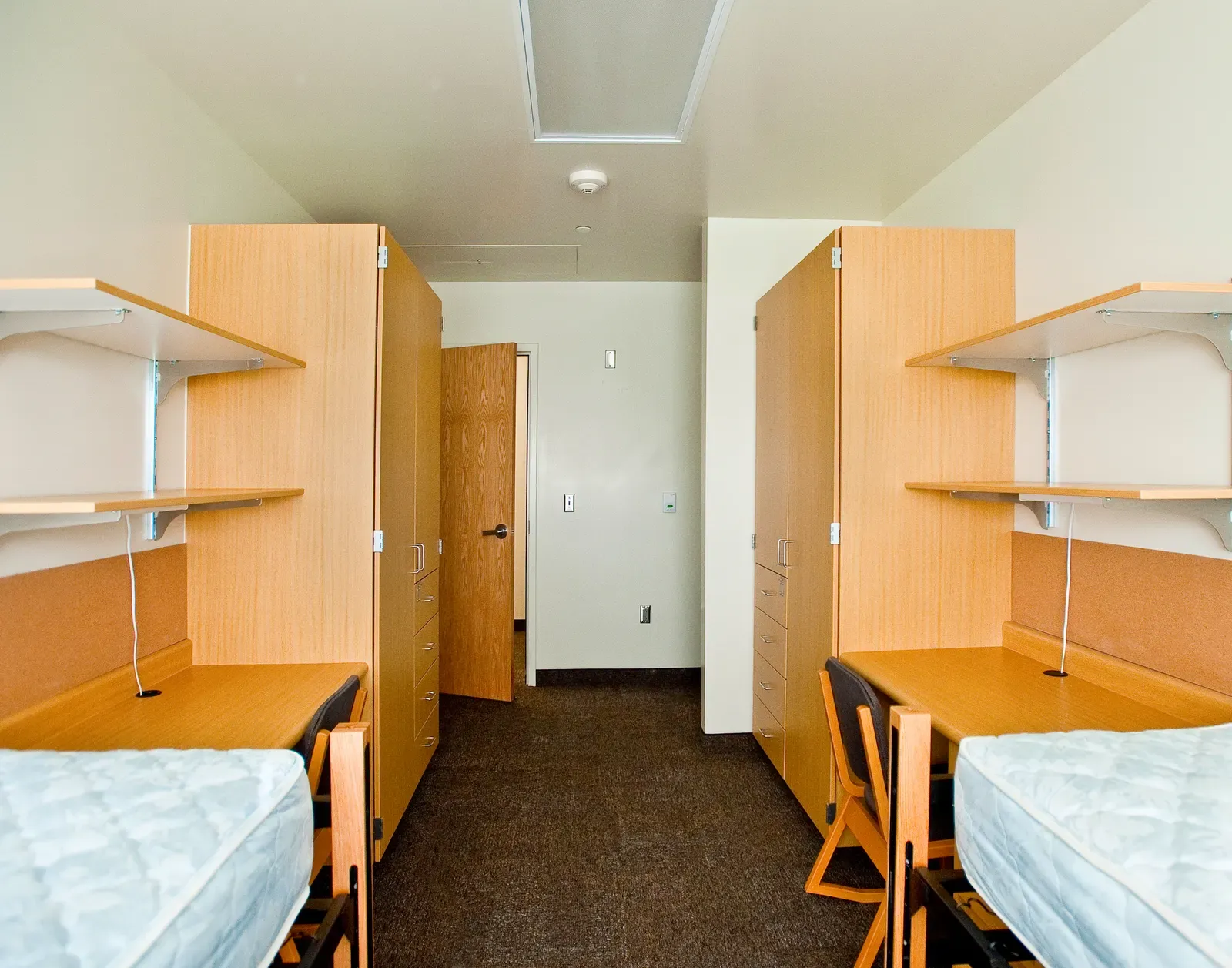 Dorm room with two beds, built-in wardrobes and desks along the walls.