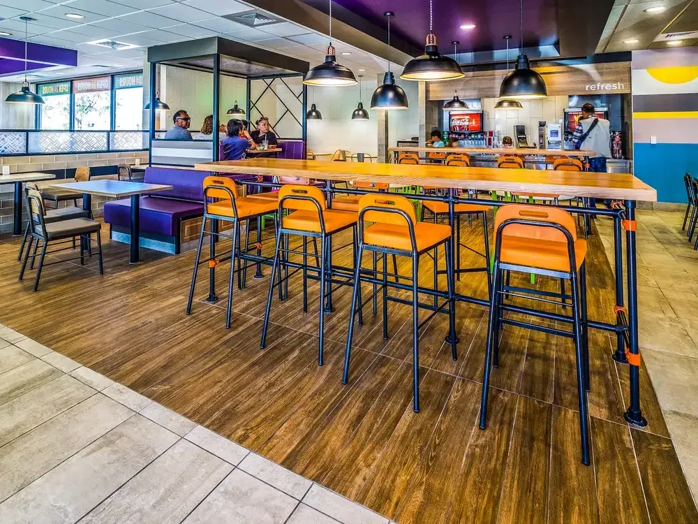 Dining room with a tall communal table, orange stools and pendant lamps.