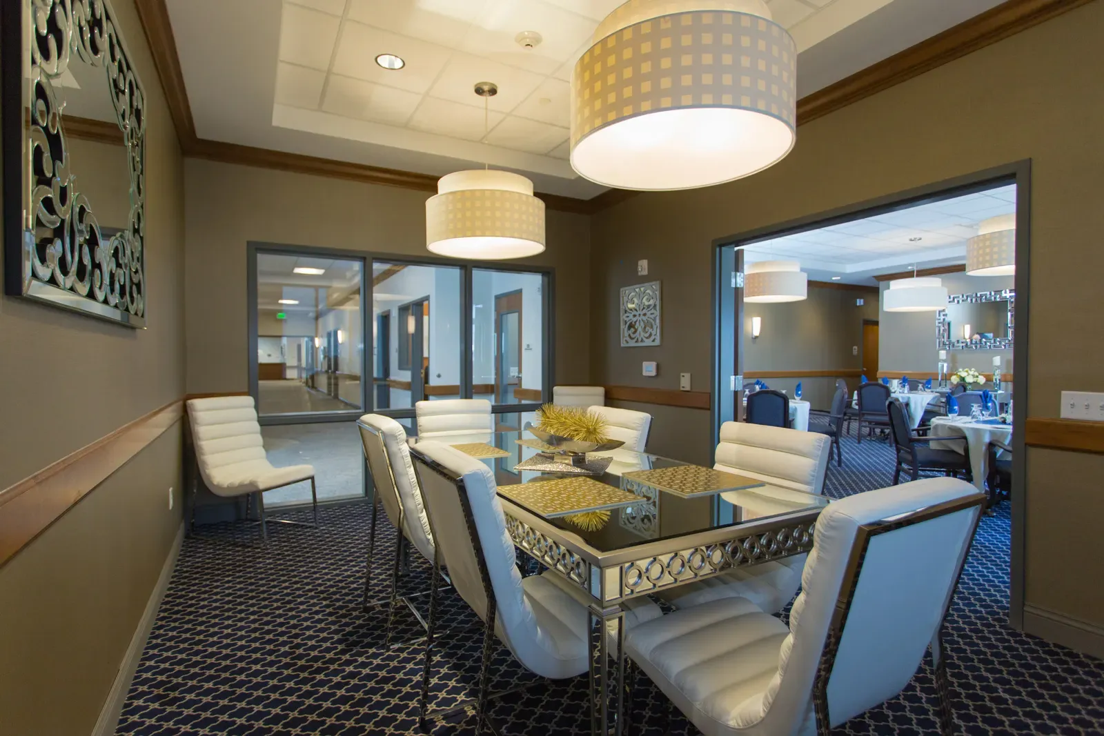 Private dining room with a mirrored table, white upholstered chairs, and pendant lights.