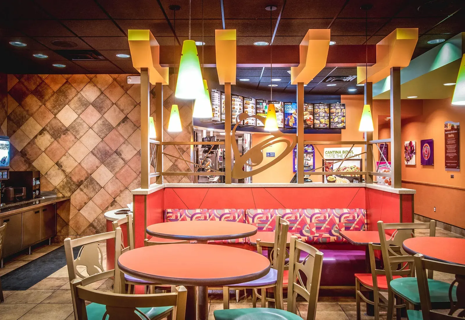 Dining area with diamond-pattern wall tile, round tables and a booth beneath yellow light fixtures